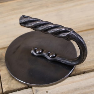 May include: A black metal hook with a twisted handle and a round base. The hook is attached to the base with three rivets.