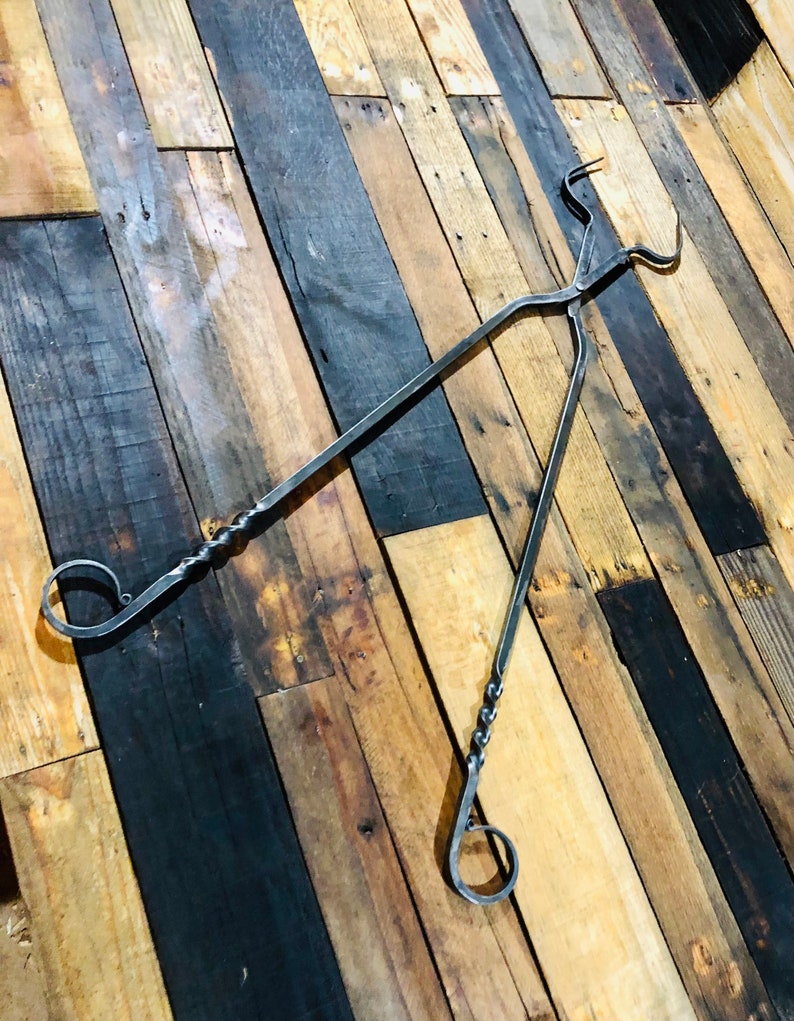 May include: A pair of black metal tongs with twisted handles. The tongs are made of forged steel and have a rustic look. They are perfect for grabbing hot items from a fire or grill.
