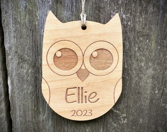 Puede incluir: Un adorno de madera en forma de búho con un corazón y el nombre "Ellie" y el año "2023" grabados en él.