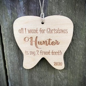 May include: A wooden tooth-shaped Christmas ornament with the text "all I want for Christmas Hunter is my 2 front teeth 2020".