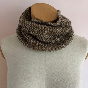 May include: A knitted cowl in brown and beige tones, shown on a mannequin. The thick knit structure is evident, giving a warm and comfortable look. The cowl is designed to be worn around the neck for warmth and fashion.