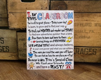 Puede incluir: Un letrero rectangular con las palabras "IN THIS CLASSROOM" en letras coloridas. El letrero presenta texto inspirador e ilustraciones de un libro infantil, perfecto para un aula o habitación infantil.