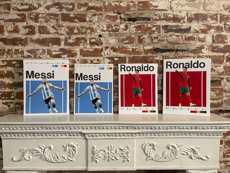 May include: Four framed prints of soccer players, two of Lionel Messi and two of Cristiano Ronaldo. The prints are on a white mantelpiece with ornate detailing. The prints feature the players in their national team jerseys, with the text "Messi" and "Ronaldo" in bold black lettering.