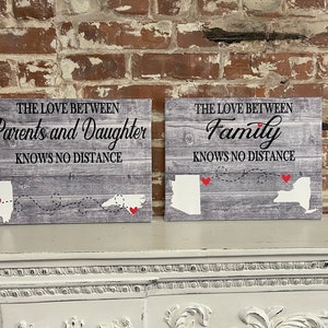 May include: Two wood signs with a gray wood grain background and white outlines of states. The signs have the text "The love between Parents and Daughter knows no distance" and "The love between Family knows no distance".