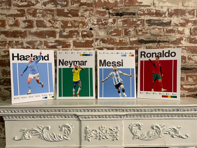 May include: Four colorful posters featuring famous soccer players: Haaland, Neymar, Messi, and Ronaldo. Each poster has a red, green, blue, or orange background with the player's name in white text at the top. The posters are displayed on a white mantel.