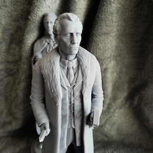 Puede incluir: Una figura gris de un hombre con un abrigo largo con cuello de piel, sosteniendo un libro y un objeto pequeño. Otra figura es visible en el fondo. El hombre lleva un traje y corbata. El tema general es una figura histórica.