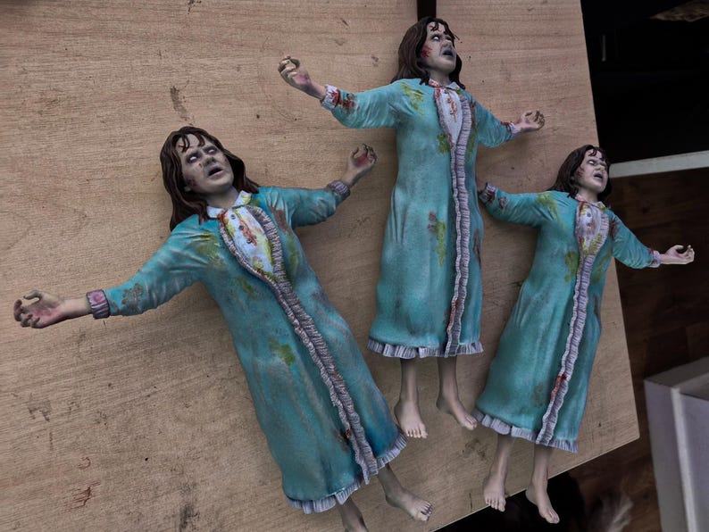 May include: Three identical figurines of a girl with dark hair, wearing a teal nightgown with a ruffled white front panel and sleeves. Each figure is posed with arms outstretched, featuring distressed fabric details and a pale, expressive facial expression.
