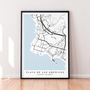 May include: A black and white map print of Playa de las Americas, Canary Islands, with a light blue background. The map shows the streets and coastline of the city.