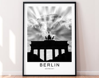 May include: Black and white photograph of the Brandenburg Gate in Berlin, Germany. The gate is silhouetted against a cloudy sky with sun rays shining through the clouds. The text "BERLIN GERMANY" is printed below the gate.