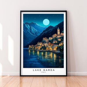Könnte beinhalten: Eine digitale Illustration einer Stadt am Ufer des Gardasees in Italien bei Nacht. Die Stadt ist mit Lichtern beleuchtet und der Mond scheint hell am Himmel. Der Text "LAKE GARDA ITALY" befindet sich am unteren Rand des Bildes.