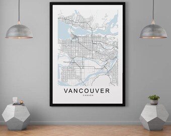 May include: Black and white line art map of Vancouver, Canada, with the city name printed below the map. The map is framed in a black frame and hanging on a gray wall. Two silver pendant lights hang above the framed map.