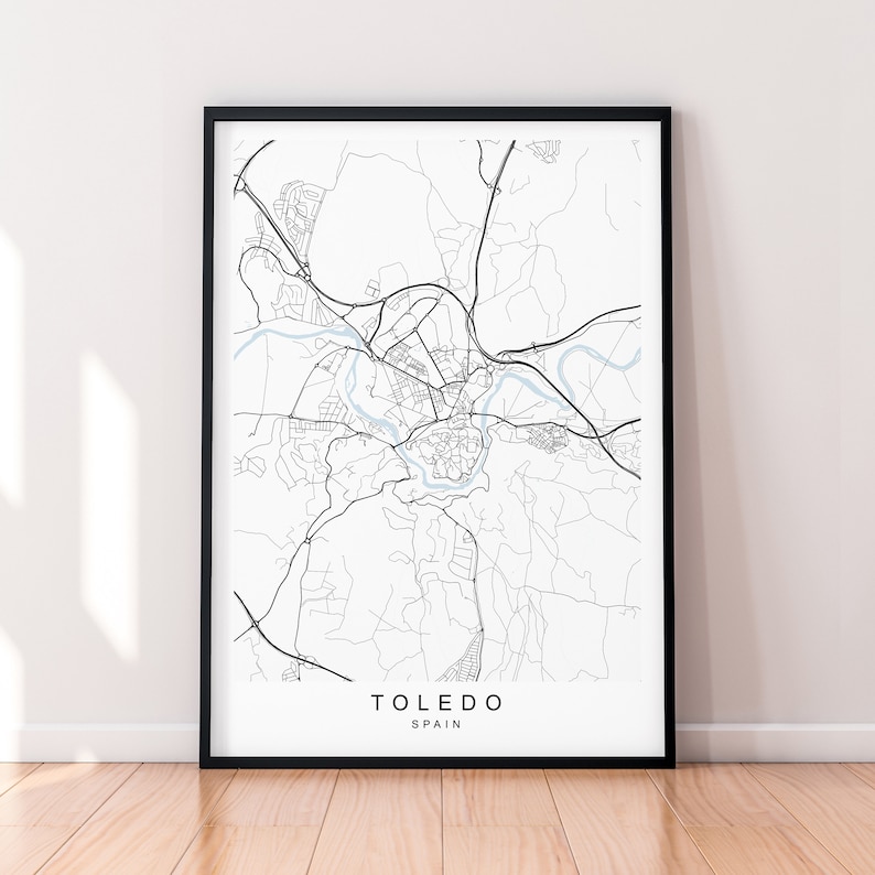 May include: A framed black and white map print of Toledo, Spain. The map features detailed street layouts, roads, and a river running through the city. The city name and country are printed in a clean, modern font at the bottom of the print.