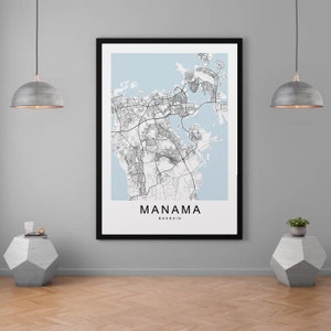 May include: A black and white map print of Manama, Bahrain, in a black frame. The map is on a light blue background. The print is hanging on a light gray wall with two gray pendant lights and two gray concrete side tables.