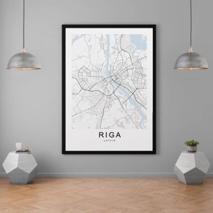 Puede incluir: Una impresión enmarcada en negro de un mapa de Riga, Letonia. El mapa está en blanco y negro con acentos azules. El nombre de la ciudad "Riga" y el nombre del país "Letonia" están impresos debajo del mapa.