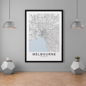 May include: A framed wall art print featuring a detailed black and white street map of Melbourne, Australia. The map displays a light blue water section, intricate road networks, and the text MELBOURNE AUSTRALIA printed in bold black capital letters.