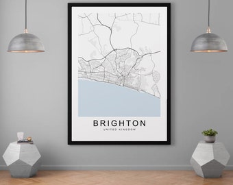 May include: A framed map print of Brighton, UK, with a black frame. The map shows a detailed street layout in black and white, with a light blue section representing the sea. The word "BRIGHTON" and "UNITED KINGDOM" are printed in black.