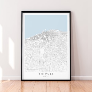 May include: A black and white map print of Tripoli, Libya. The map shows the city's streets and landmarks. The print is framed in a black frame and has a light blue background.
