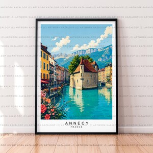May include: A framed art print depicting the Palais de l'Île in Annecy, France, featuring a stone building surrounded by turquoise water, colourful buildings along the canal, vibrant flowers in the foreground, and mountains under a blue sky.