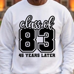 May include: A white long-sleeve sweatshirt featuring a black graphic print on the chest. The text reads "class of 83" in a cursive script above large block numbers "83" and the phrase "45 YEARS LATER" in a bold, sans-serif font below.