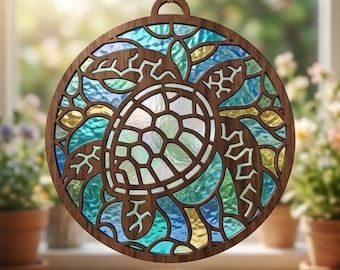Puede incluir: Un adorno colgante circular de madera con la silueta de una tortuga marina cortada con láser. El diseño está relleno con paneles de vidrio texturizado translúcido en tonos azul, turquesa y amarillo, creando un efecto de vitral.
