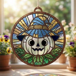 May include: A circular stained glass suncatcher featuring a white pumpkin wearing a blue witch hat. The design is encased in a dark wood frame with a hanging loop at the top. The glass panels display shades of blue, yellow, and green.