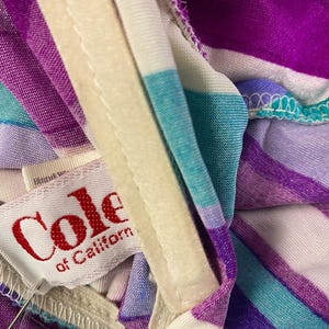 May include: Close-up of a vintage garment with a striped pattern in shades of purple, teal, and white. The label reads "Cole of California" in red lettering. The fabric is soft and appears to be a lightweight material.