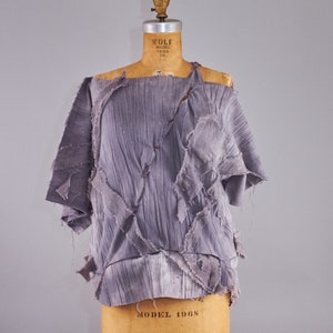 May include: A grey, off-the-shoulder top made of fabric with a distressed, layered look. The top is on a dress form.