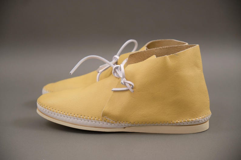 Pu&ograve; includere: Un paio di stivaletti alla caviglia in pelle giallo chiaro con lacci bianchi. Gli stivaletti hanno una suola cucita e una finitura liscia. I lacci sono annodati. Questi stivaletti sono progettati per il comfort e lo stile.