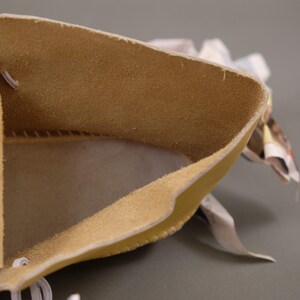 Pu&ograve; includere: Primo piano di un astuccio in pelle beige con un interno morbido e strutturato. I bordi sono ripiegati, rivelando l'interno dell'astuccio. &Egrave; visibile un filo bianco. Lo sfondo &egrave; grigio neutro.