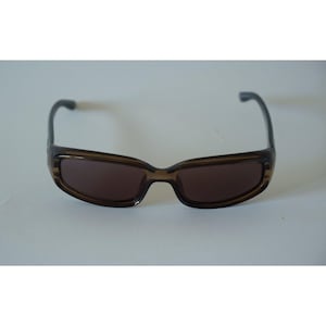 May include: Brown sunglasses with a rectangular frame and dark lenses. The sunglasses have a sleek, modern design, suitable for everyday wear. The arms are a darker shade of brown.