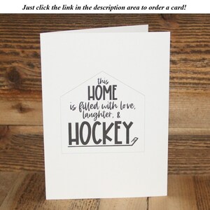 May include: A white card with black text that reads "this HOME is filled with love, laughter, & HOCKEY". The text is in a house shape with a hockey stick underneath.