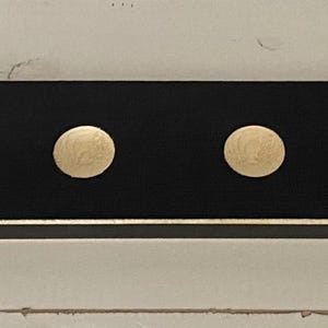 May include: A rectangular black wooden coat rack with seven evenly spaced, gold-colored knobs. The rack has a thin gold trim along the bottom edge and is mounted on a white wooden surface.