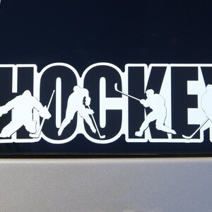 以下が含まれることがあります： 黒と白のステッカーに、太字で「HOCKEY」という文字が書かれています。ステッカーには、スティックとパックを持ったシルエットのホッケー選手が5人描かれています。