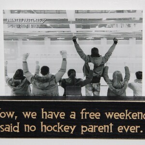 May include: Black wooden sign with white text that reads "Wow, we have a free weekend," said no hockey parent ever."  The sign has a black and white photo of people cheering at a hockey game.