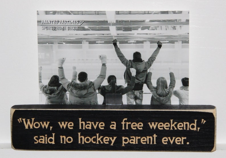 May include: Black wooden sign with white text that reads "Wow, we have a free weekend," said no hockey parent ever."  The sign has a black and white photo of people cheering at a hockey game.