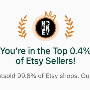May include: A digital graphic featuring a circular logo with the word HOCKEY, flanked by orange laurel branches. Below, dark green text reads: You're in the Top 0.4% of Etsy Sellers! Light gray text below states: You've outsold 99.6% of Etsy shops. Outstanding!