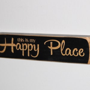 May include: Black wooden sign with the text "this is my Happy Place" in a light wood color.
