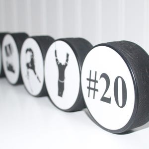 May include: A row of black and white hockey pucks with different designs. The last puck has the number 20 printed on it.