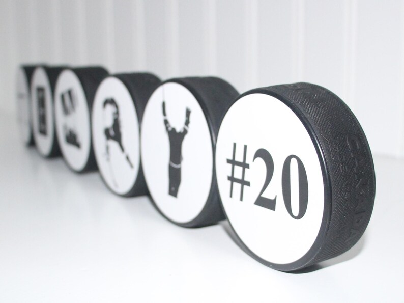 May include: A row of black and white hockey pucks with different designs. The last puck has the number 20 printed on it.