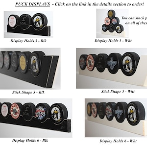 May include: Four different hockey puck displays, each with a different number of slots and color. The displays are made of wood and have a black or white finish. The text "You can stack pucks on all of these!" is visible in the top right corner of the image.