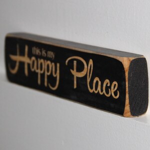 May include: Black wooden sign with the text "This is my Happy Place" in white lettering.