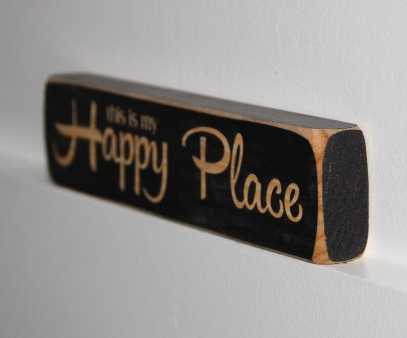 May include: Black wooden sign with the text "This is my Happy Place" in white lettering.