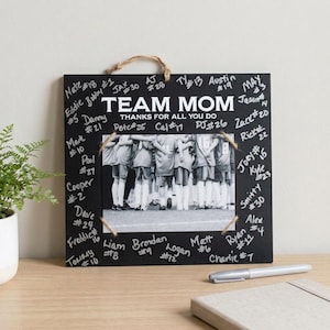 May include: A black square wooden sign with a central black and white photograph of a sports team. The text reads TEAM MOM THANKS FOR ALL YOU DO. The border is covered in handwritten names and jersey numbers in white ink, with a jute rope hanger.