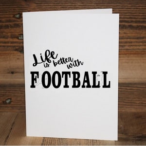 May include: A white card with black text that reads "Life is better with FOOTBALL".