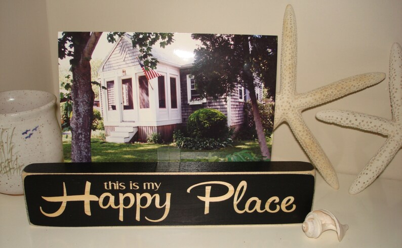 May include: Black wooden sign with white lettering that reads "this is my Happy Place". The sign is sitting on a table with a seashell and a starfish.