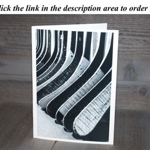 May include: Black and white photograph of a stack of hockey sticks. The sticks are arranged in a vertical stack, with the blades facing the viewer. The sticks are all the same size and shape, and they are all made of wood. The photograph is taken from a low angle, so that the viewer can see the full length of the sticks.