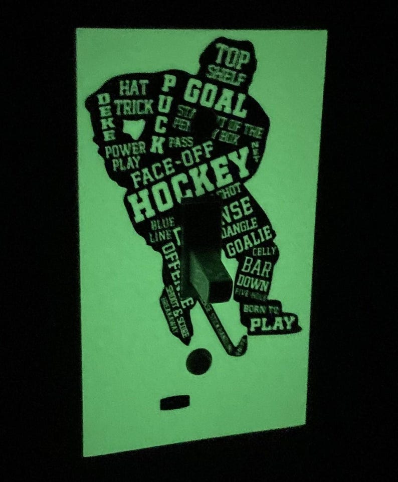 K&ouml;nnte beinhalten: Ein im Dunkeln leuchtender Lichtschalter-Aufkleber mit einer Hockeyspieler-Silhouette. Die Silhouette besteht aus Hockeybegriffen wie "Tor", "Face-Off", "Blaue Linie", "Abseits", "Schie&szlig;en & Punkten", "Geboren zum Spielen" und "Oben auf dem Regal".