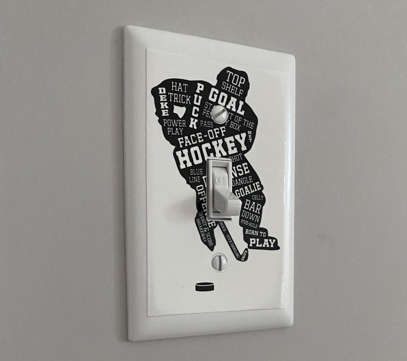 K&ouml;nnte beinhalten: Ein wei&szlig;er Lichtschalter mit einer schwarzen Silhouette eines Hockeyspielers. Die Silhouette besteht aus Hockeybegriffen wie "Tor", "Face-Off", "blaue Linie" und "geboren zum Spielen".