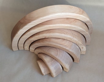May include: A set of six wooden rainbow arches, stacked in a crescent shape. The arches are made of natural wood and are unfinished.