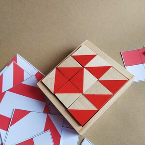 Puede incluir: Un marco de madera contiene nueve bloques geom&eacute;tricos rojos y blancos, dispuestos en un patr&oacute;n. Los bloques son de madera y tienen un patr&oacute;n geom&eacute;trico rojo y blanco en cada lado.